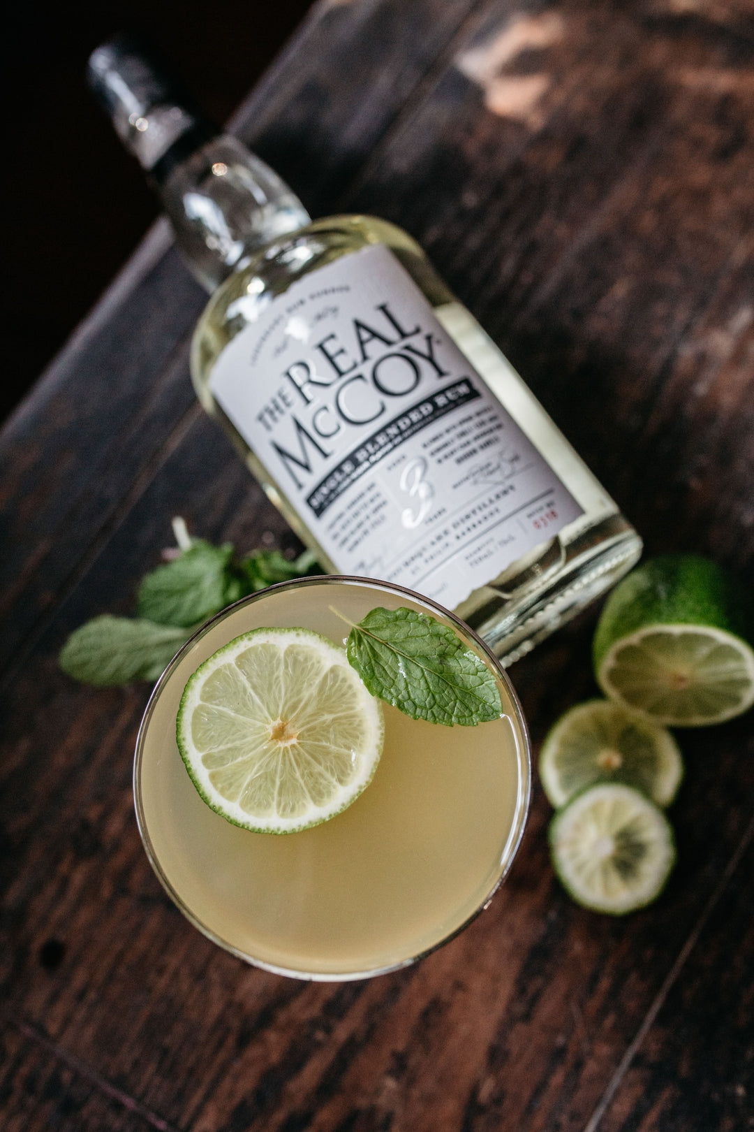 Picture of mojito cocktail in coupe glass with real mccoy 3 year aged rum bottle behind