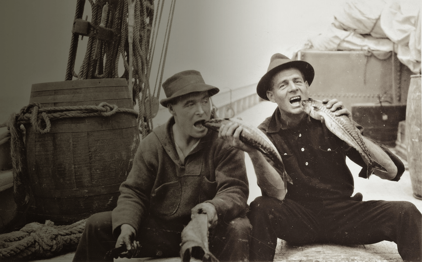 Bill McCoy and crew member pretending to bite the head of fish they caught on board McCoy's boat Arethusa