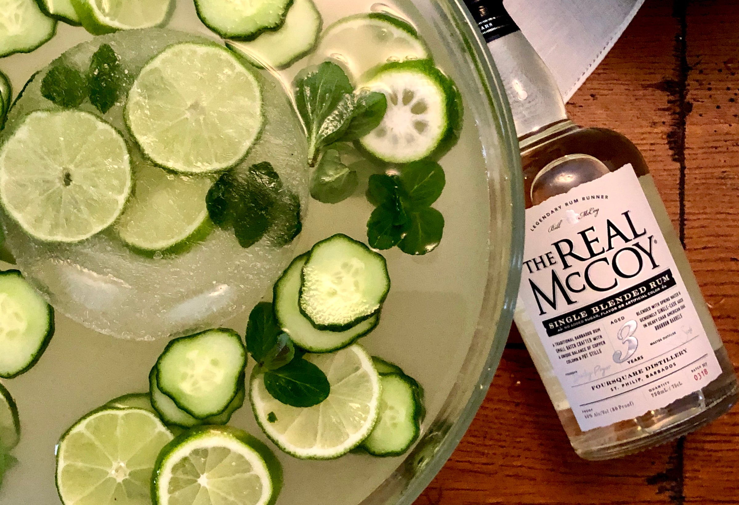 Mojito in punch bowl with cucumber, lime slices and mint leaves floating, Real McCoy Rum bottle on table