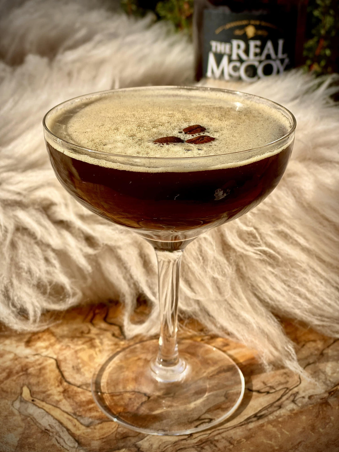 Espresso rumtini with 3 coffee beans floating on top and bottle of Real McCoy 12 year aged rum in the background